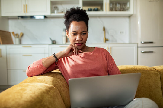 Woman using laptop on sofa in home kitchen