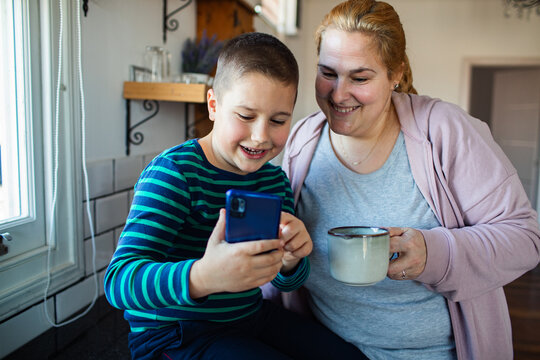 Mother and son using smartphone in kitchen at home
