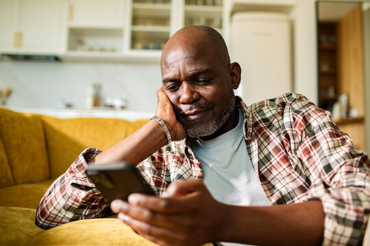 Mature man using smartphone at home on sofa