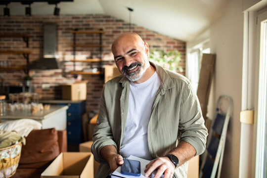 Smiling middle-aged man unpacking boxes in home kitchen