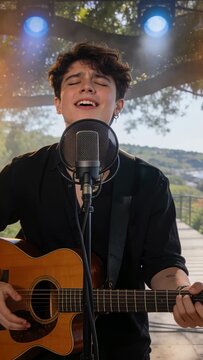 Vertical video: Strumming singer in black shirt playing guitar into mic after light cue, deck haze