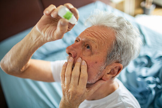 Senior man applying eye drops at home