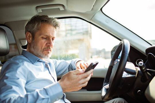 Mature driver using smartphone in car interior