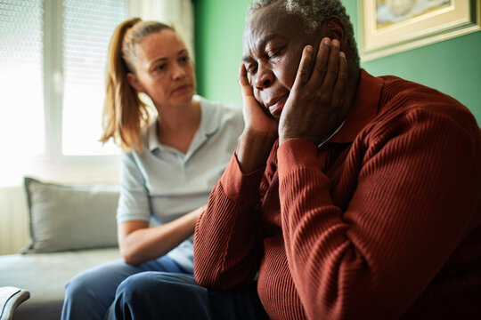 Caregiver comforting stressed senior man at home