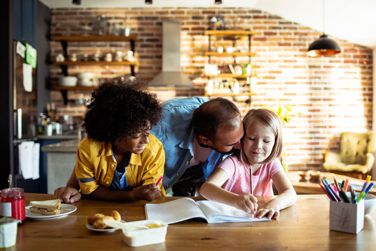 Parents helping daughter with drawing at home kitchen table