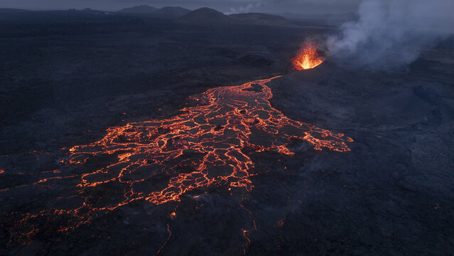 Aerial view of an active volcano eruption with glowing lava flows spreading across the dark volcanic landscape in Reykjavik, Reykjavikurborg, Iceland.