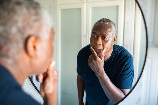Older man examining face in bathroom mirror