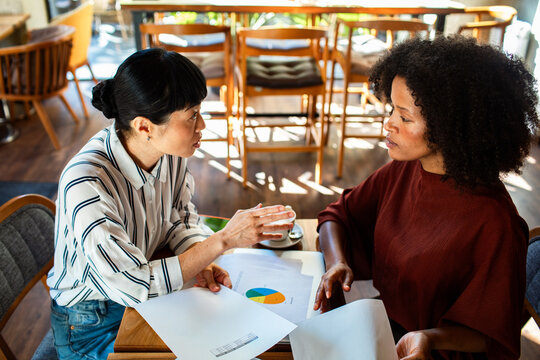 Two businesswomen discussing financial charts at cafe