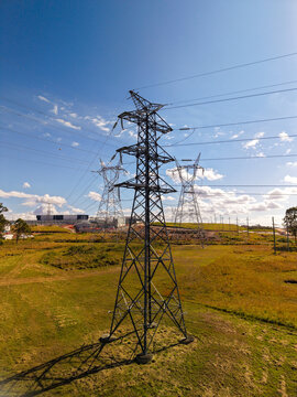 Aerial view of power transmission lines and electrical transformers set in a grassy field under a clear blue sky in Brendale, Queensland, Australia.