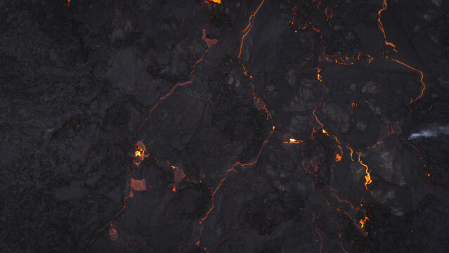 Aerial view of glowing lava flowing through dark volcanic rock fissures in a rugged landscape in Reykjavik, Reykjavikurborg, Iceland.