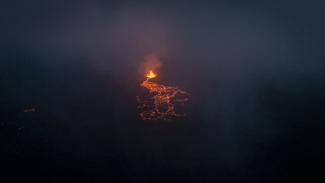 Aerial view of a glowing volcanic eruption at night with molten lava flowing through dark smoke and volcanic ash in Reykjavik, Reykjavikurborg, Iceland.