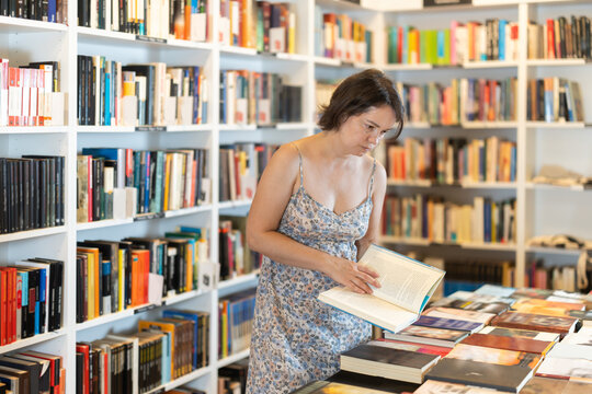 Adult female reader explores aisles of bookstore, looking for new title to enjoy