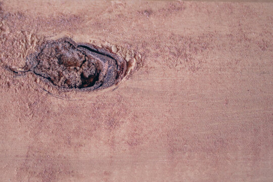 Wood plank displaying a prominent knot and visible grain, showcasing a rustic, rough texture and natural brown tones, perfect for an aged background or surface