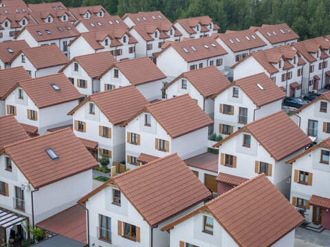 Aerial view of a modern residential neighborhood featuring rows of houses with red tiled roofs, white facades, and wooden window frames in Poland.
