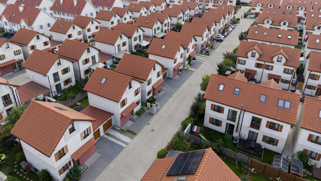 Aerial view of a modern residential neighborhood with white houses featuring red tiled roofs, organized along paved streets in Poland.