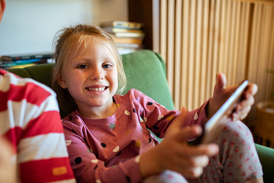 Smiling girl using smartphone at home on sofa