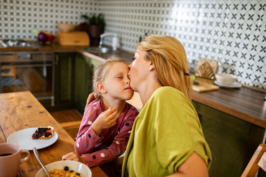 Mother kissing daughter during breakfast in a home kitchen