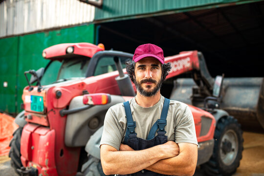 Confident farmer standing by red tractor in barn