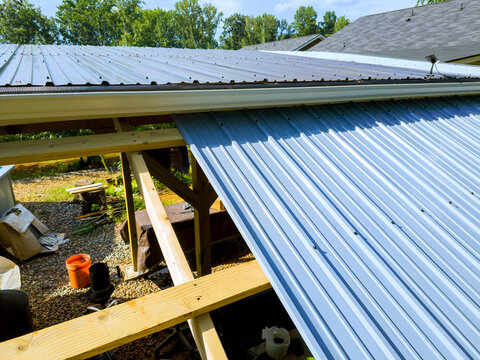 Putting up metal roof on wooden frame in backyard, tools materials on ground.