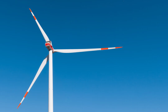 Aerial view of a white wind turbine with orange-tipped blades standing against a clear blue sky in Uckermark, Brandenburg, Germany.
