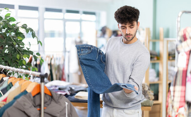 Fototapeta premium Young man buyer choosing jeans in clothing store