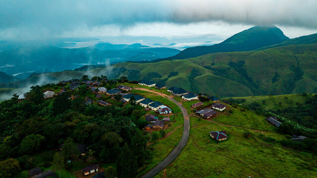 Aerial view of Obudu Mountain Resort with scattered chalets nestled among lush green rolling hills and a winding road under a cloudy sky in Obudu, Cross River, Nigeria.