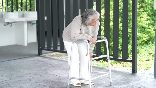 Elderly woman using walker with knee pain on outdoor patio, mobility aid for senior care, rehabilitation and healthcare recovery, leaning forward holding leg, improving balance near garden walkway