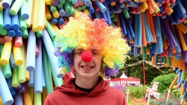 Happy teenage boy wearing colorful rainbow clown wig at festival outdoors