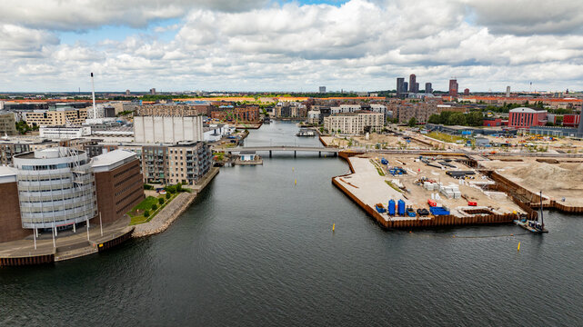 Aerial view of the harbor area featuring modern architecture, a bridge, and ongoing construction sites along the waterfront in Copenhagen, Denmark.