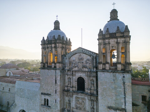 Aerial view of the Templo de Santo Domingo de Guzman with its iconic twin bell towers and tiled domes illuminated by the soft light of sunrise in Oaxaca, Oaxaca, Mexico.