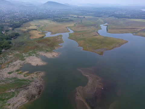 Aerial view of a winding river flowing through a vast landscape with green fields, hills, and calm water in Jalapa, Oaxaca, Mexico.