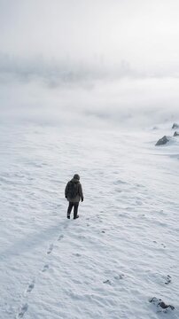 Person Walking Alone Through a Snowy Landscape with Low Visibility and Distant City Skyline