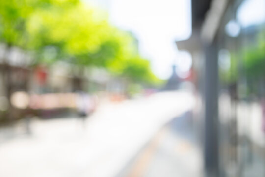 Abstract blurred modern urban plaza background with a building frontage and green trees