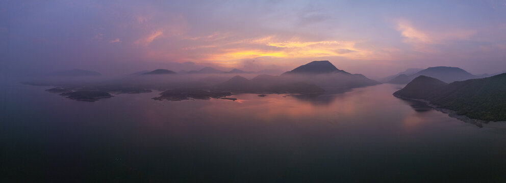 Aerial view of a serene lake surrounded by misty mountains during a vibrant sunrise in Jalapa, Oaxaca, Mexico.