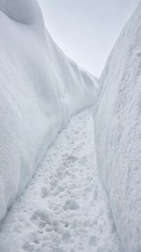 Narrow Snow Covered Pathway Between Tall Snow Walls on a Cloudy Winter Day
