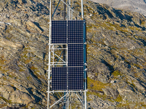 Aerial view of solar panels mounted on a metal tower structure against a rugged, rocky mountain slope in Valldal, More og Romsdal, Norway.