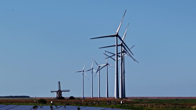 Aerial view of modern turbines traditional windmill and rows of solar panels spread across flat Dutch countryside in Groningen Netherlands