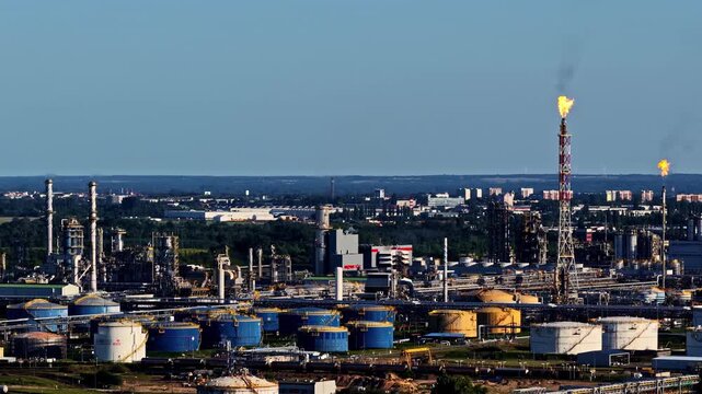 ORLEN Płock Production Plant and PKN Orlen Refinery stretch across the frame with tanks, chimneys and burning flare stacks under clear blue sky.