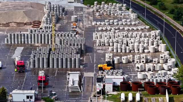 Aerial sideways shot reveals rows of stacked concrete pipes and culvert rings at a precast manufacturing yard with trucks and sand piles