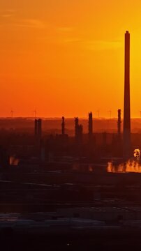 ORLEN Płock refinery silhouettes and distant wind turbines glow beneath orange sunset