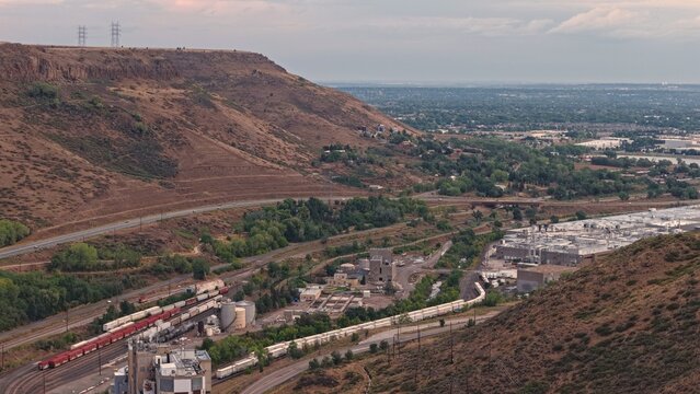 Aerial view of the Coors Brewery facility in the valley, featuring industrial buildings, railway tracks with freight trains, and rugged terrain in Golden, Colorado, United States.