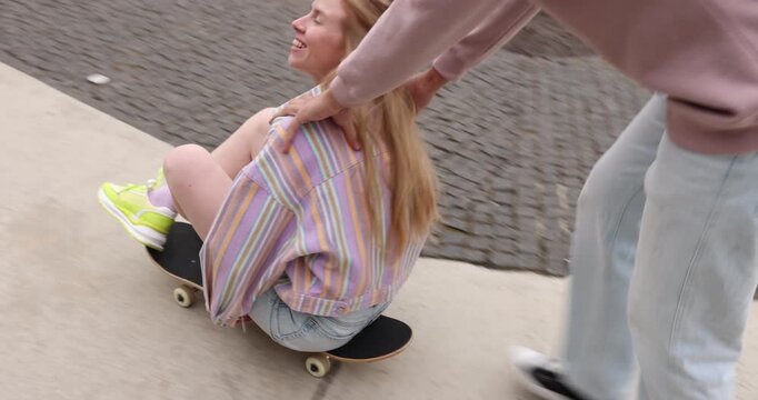 Man pushing his girlfriend on skateboard outdoors