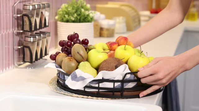 Woman putting basket with various fresh fruits onto countertop indoors, closeup. Camera tracking