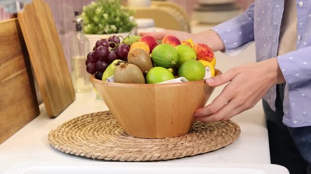 Woman with bowl of various fresh fruits at countertop indoors, closeup