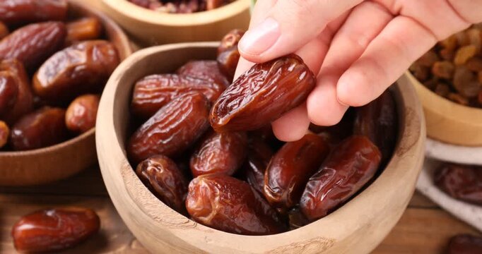 Woman taking tasty dried date from bowl at wooden table, closeup