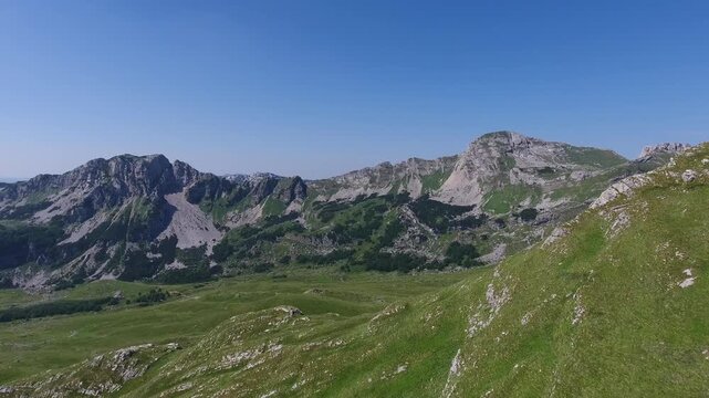 Aerial view of Bobotov Kuk, the highest peak in the Durmitor mountain range, featuring rugged rocky summits and lush green slopes in Zabljak Municipality, Montenegro.