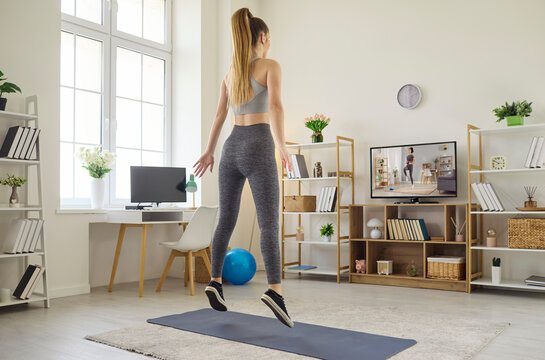 Woman home workout on tv with online training. She jumps vertically on a mat, following a coach on the television for exercise to boost cardio and leg strength. Concept of energetic home fitness