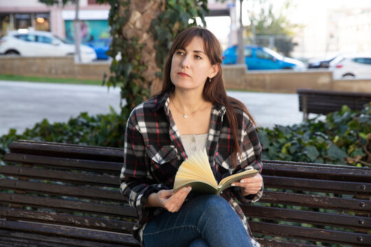 A woman is relaxing in a park with a book, with space for text nearby.