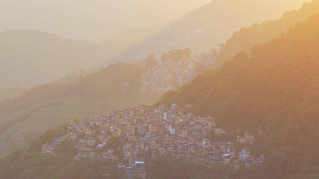 Aerial view of a traditional village nestled in the mountains during golden hour in Honghe Hani and Yi Autonomous Prefecture, Yunnan, China.