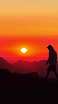 Silhouetted hiker stands on a rocky ridge at Col d'Aubisque watching the vivid orange sun set over layered mountain peaks.